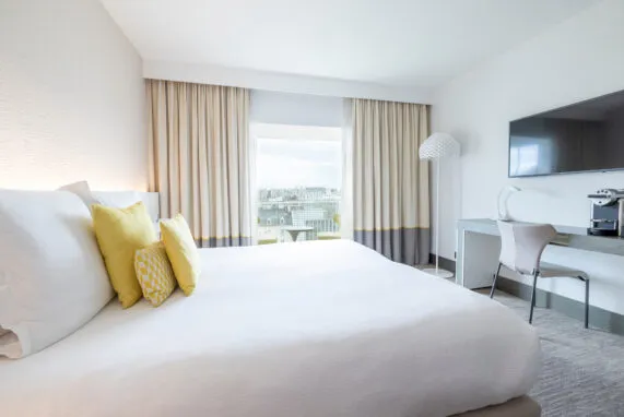 Wide view of a Deluxe room with its amenities: desk, lounge area, bow window and coffee machine. Carefully curated decor.