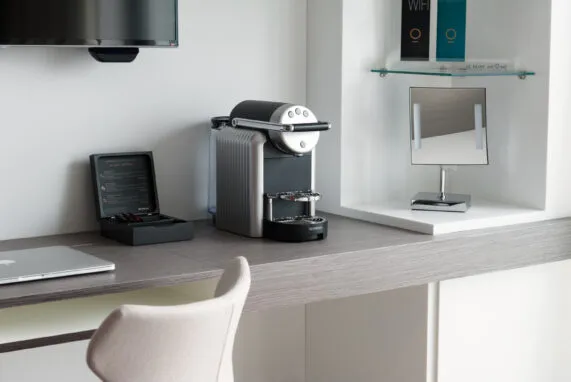 Wide view of an Executive room with full amenities: desk, lounge area and coffee machine. A soft and soothing atmosphere.