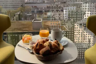 Close-up of coffee, pastries and orange juice on the table in the bow-window lounge area, with panoramic city views.