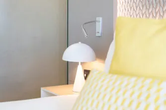 Close-up of the headboard and bedside table in a hotel room, with colorful designer cushions in a calm and comfortable atmosphere.