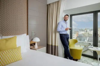 Smiling businessman enjoying a coffee while standing in the lounge area of his room, in a calm and elegant atmosphere.