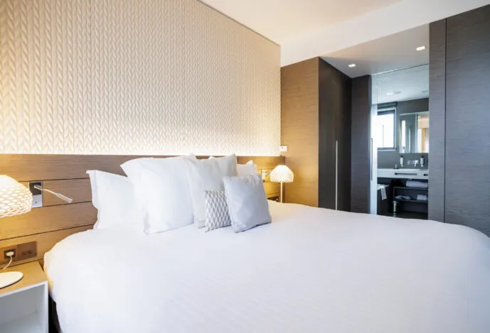 View of the Saint-Antoine suite with a king-size bed in the foreground and the bathroom visible in the background.