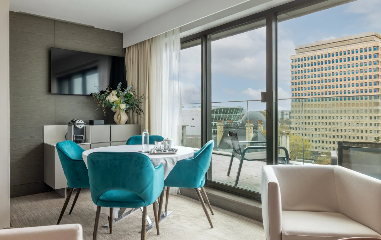 Suite lounge with tables and chairs. Large bay windows open onto one of the private terraces with outdoor seating.