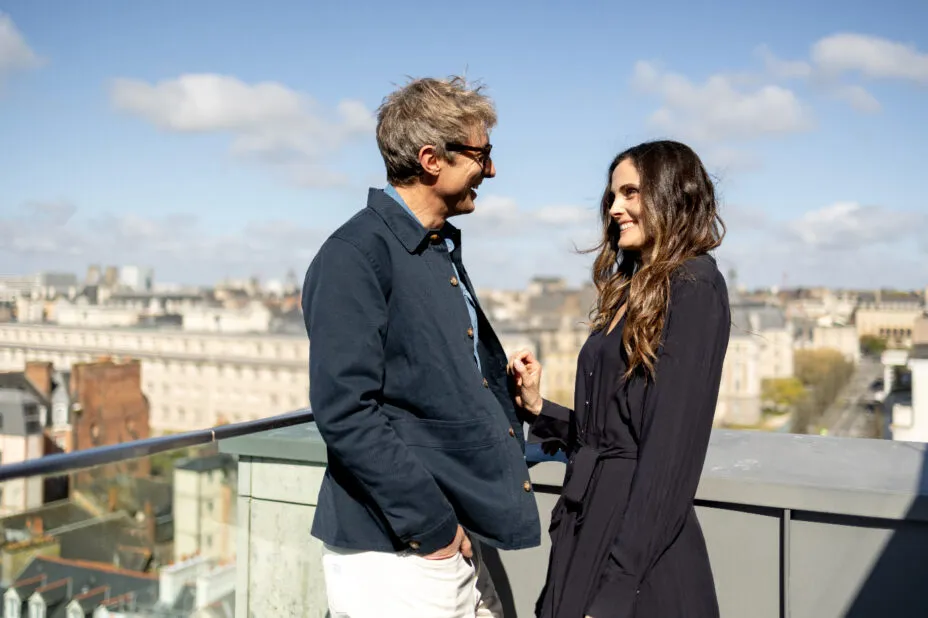 Smiling couple standing in the sunshine on the terrace of their Saint-Antoine suite, with the city in the background.