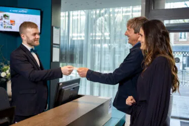 Couple souriant à la réception de l’hôtel recevant la clé de leur chambre des mains du réceptionniste.