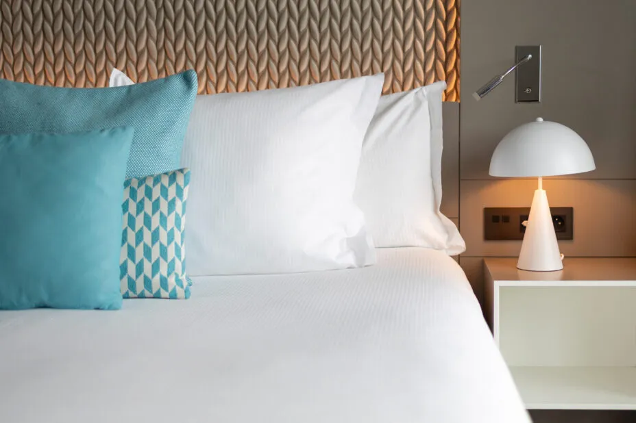 Close-up of the hotel's headboard with comfortable cushions and pillows, elegant padding and a lit bedside lamp.