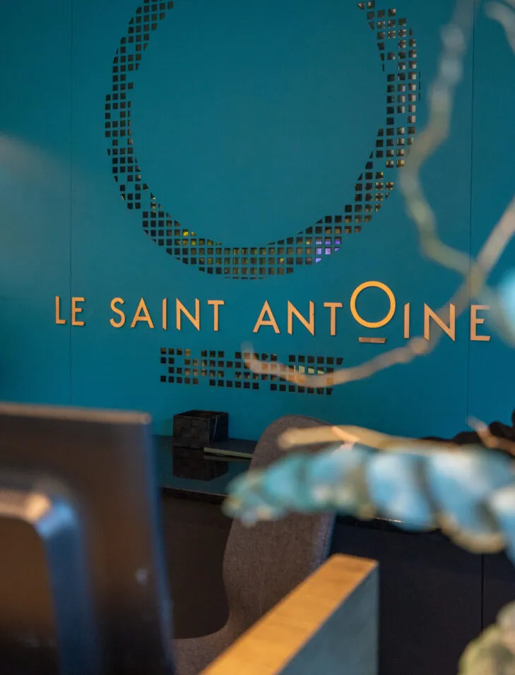 Gros plan sur le mur bleu de la réception de l’hôtel avec le logo du Saint Antoine en doré.