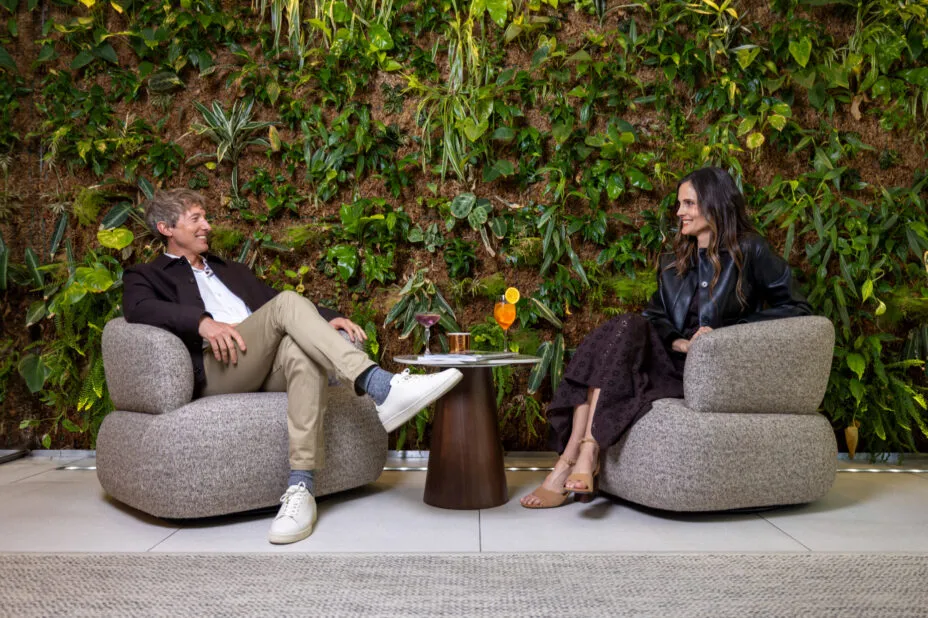 Couple souriant assis dans de larges fauteuils en tissu devant le mur végétal du bar lounge.