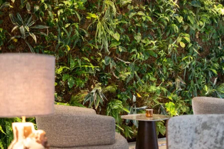 Gros plan sur les tables basses et fauteuils du bar lounge de l’hôtel devant le mur végétal.