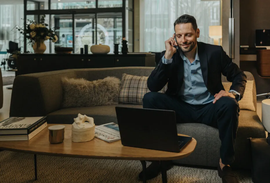 Homme d’affaires au téléphone assis sur le canapé de l’hôtel, regardant son ordinateur portable.