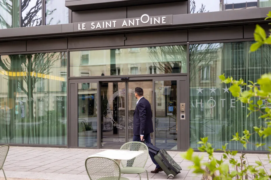 Businessman arriving in front of the hotel in the street with a rolling suitcase.