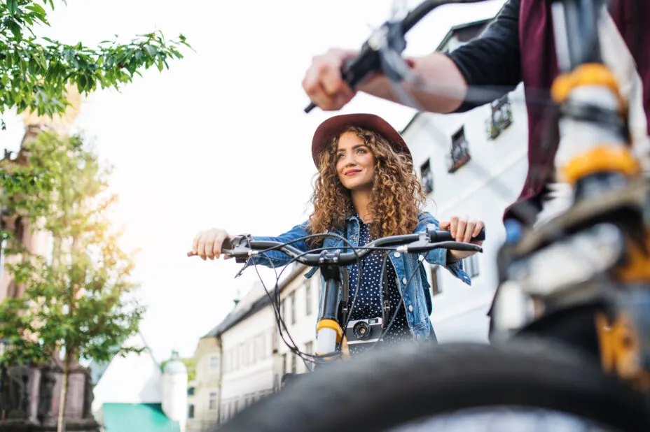 Person on a bicycle with a camera around their neck riding through the city, with another bicycle slightly out of focus in the foreground.