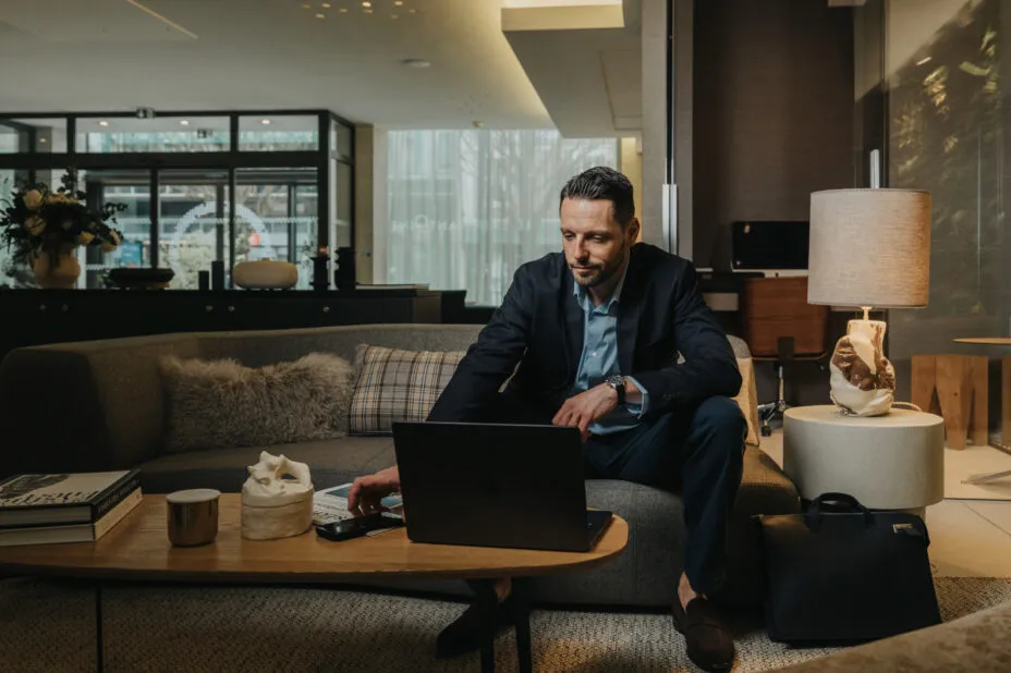 Businessman seated on a sofa in the hotel lobby, working on his laptop in a calm and cozy atmosphere.