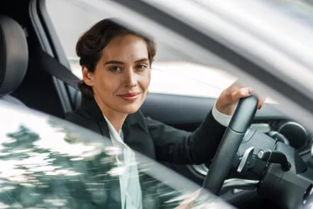 Smiling woman behind the wheel of a car, seen from outside through the window.