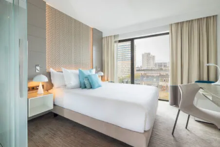 Vue d’ensemble d’une chambre Classique de l’hôtel avec lit, bureau et baie vitrée, décor beige et bleu aux couleurs douces, ambiance de confort et de sérénité.