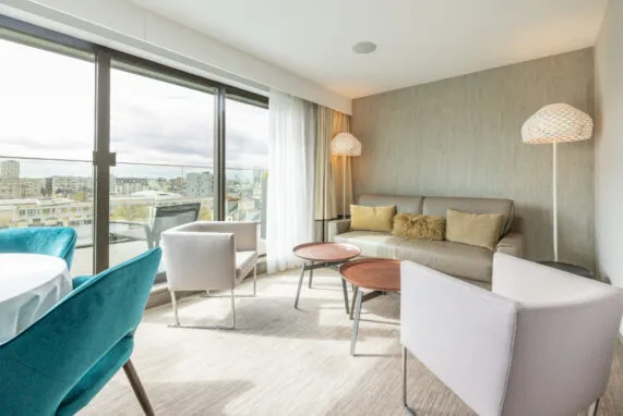 Salon de la suite Saint‑Antoine avec canapé-lit et deux fauteuils. De larges baies vitrées ouvrent sur une terrasse privée surplombant la ville.