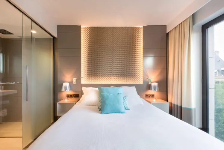 Une des chambres de l'hôtel Spa Le Saint-Antoine à Rennes, avec le lit vue de face et, d'un côté, une large baie vitrée, de l'autre, la salle de douche.