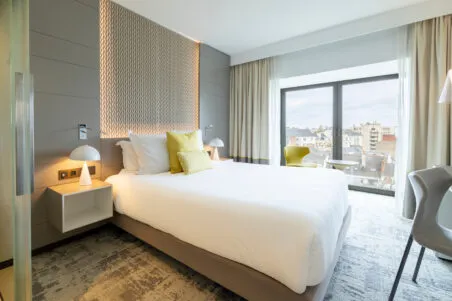 Vue d’ensemble de la chambre Exécutive de l’hôtel avec grand lit, bureau et baie vitrée, ambiance douce et feutrée.