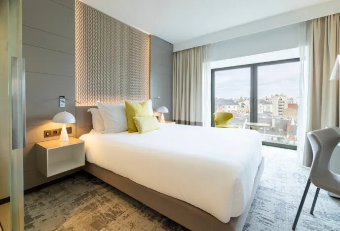 Vue d’ensemble de la chambre Exécutive de l’hôtel avec grand lit, bureau et baie vitrée, ambiance douce et feutrée.