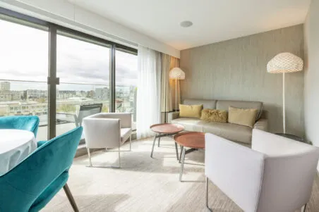 Salon de la suite Saint‑Antoine avec canapé convertible et fauteuils. De larges baies vitrées ouvrent sur une terrasse privative.