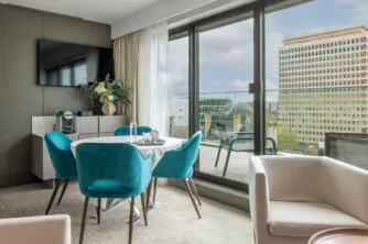 Vue du salon avec tables et chaises. De larges baies vitrées donnent sur la terrasse privée et son salon de jardin.