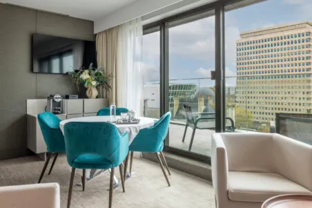 Vue du salon avec tables et chaises. De larges baies vitrées donnent sur la terrasse privée et son salon de jardin.