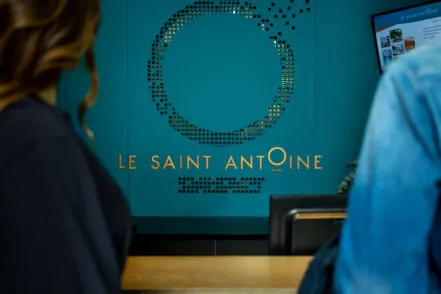 Partial rear view of a couple at the hotel reception, with the Saint-Antoine logo visible on the wall.