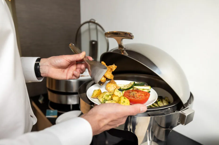 Gros plan sur les mains d’un homme se servant au buffet chaud du petit déjeuner de l’hôtel.