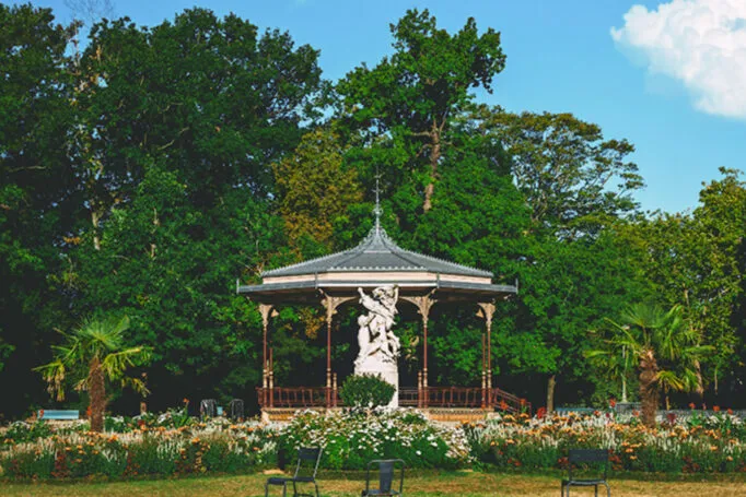Kiosque à musique du parc du Thabor à Rennes, avec statue et massifs de fleurs au premier plan et arbres en arrière-plan.
