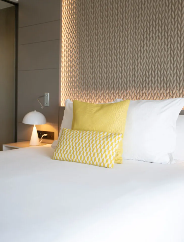 Gros plan sur un lit de l'hôtel, avec coussins confortables et tête de lit en tissu.
