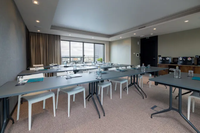 Salle de séminaire de l’hôtel vide, aménagée en configuration salle de classe prête à accueillir des participants.
