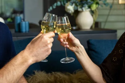 Gros plan sur les mains d’un homme et d’une femme trinquant avec des coupes dans le salon de l’hôtel.