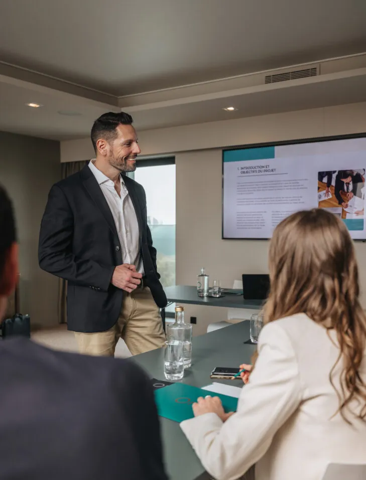 Seminar host standing and interacting with participants in a hotel meeting room.