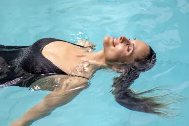 Une femme souriante flotte sur le dos dans la piscine, les yeux fermés.