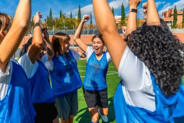 Joueuses sur terrain de sport gazonné, exultant les bras levés au ciel.