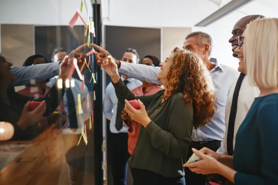 Groupe de collègues souriants devant un tableau, collaborant pour résoudre une énigme.