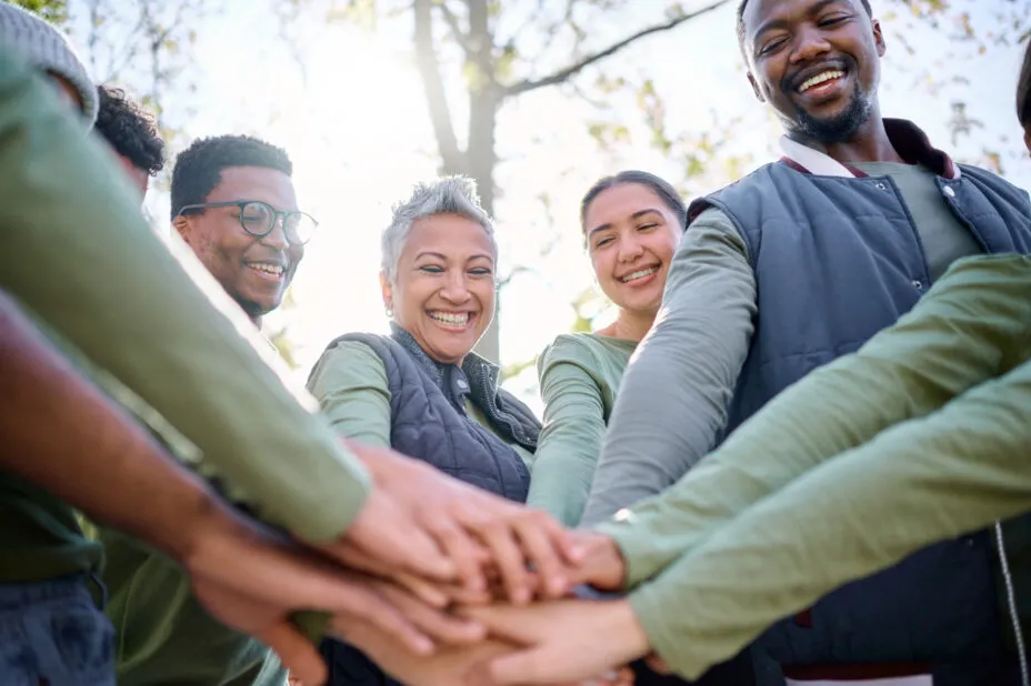 Groupe de collègues souriants en extérieur, superposant leur main en signe d'unité et de cohésion.