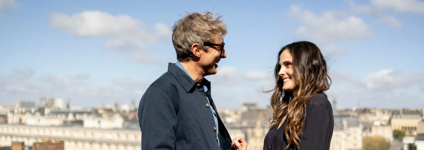 Couple complice profitant du soleil sur la terrasse du dernier étage de l’hôtel, avec vue panoramique sur les toits de Rennes.